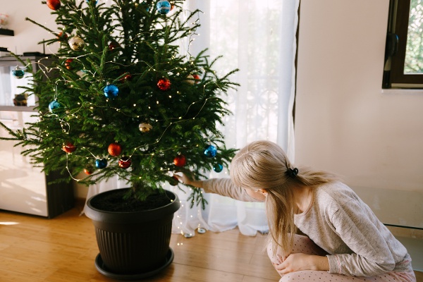 Blonde haired woman hanging ornaments on the low angle of the Christmas tree in her living room