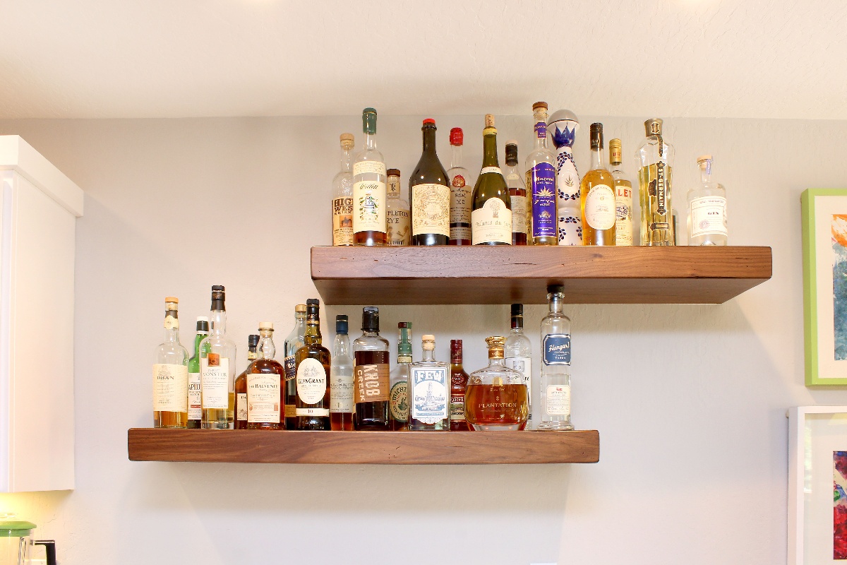 Floating kitchen shelves that feature many different types of alcohol