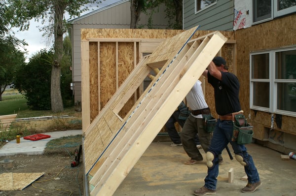 Two contractors working together to push up a studded wall of a home