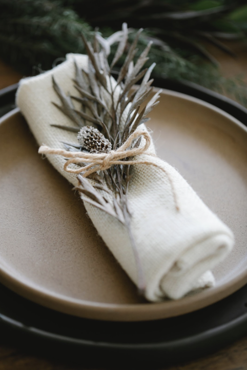Close up picture of a napkin rolled up and bound with twine and a holiday decorative garnish
