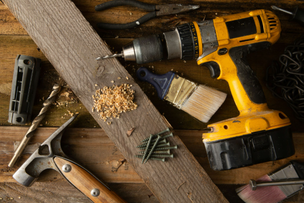 Numerous carpentry and woodworking tools laid out on a table. Power drill, hammer, screws, brush and more