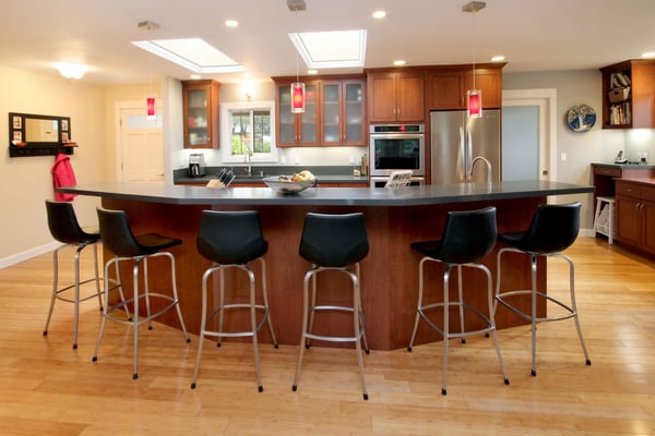 Large curved kitchen island with six bar stool chairs and two skylights for natural light