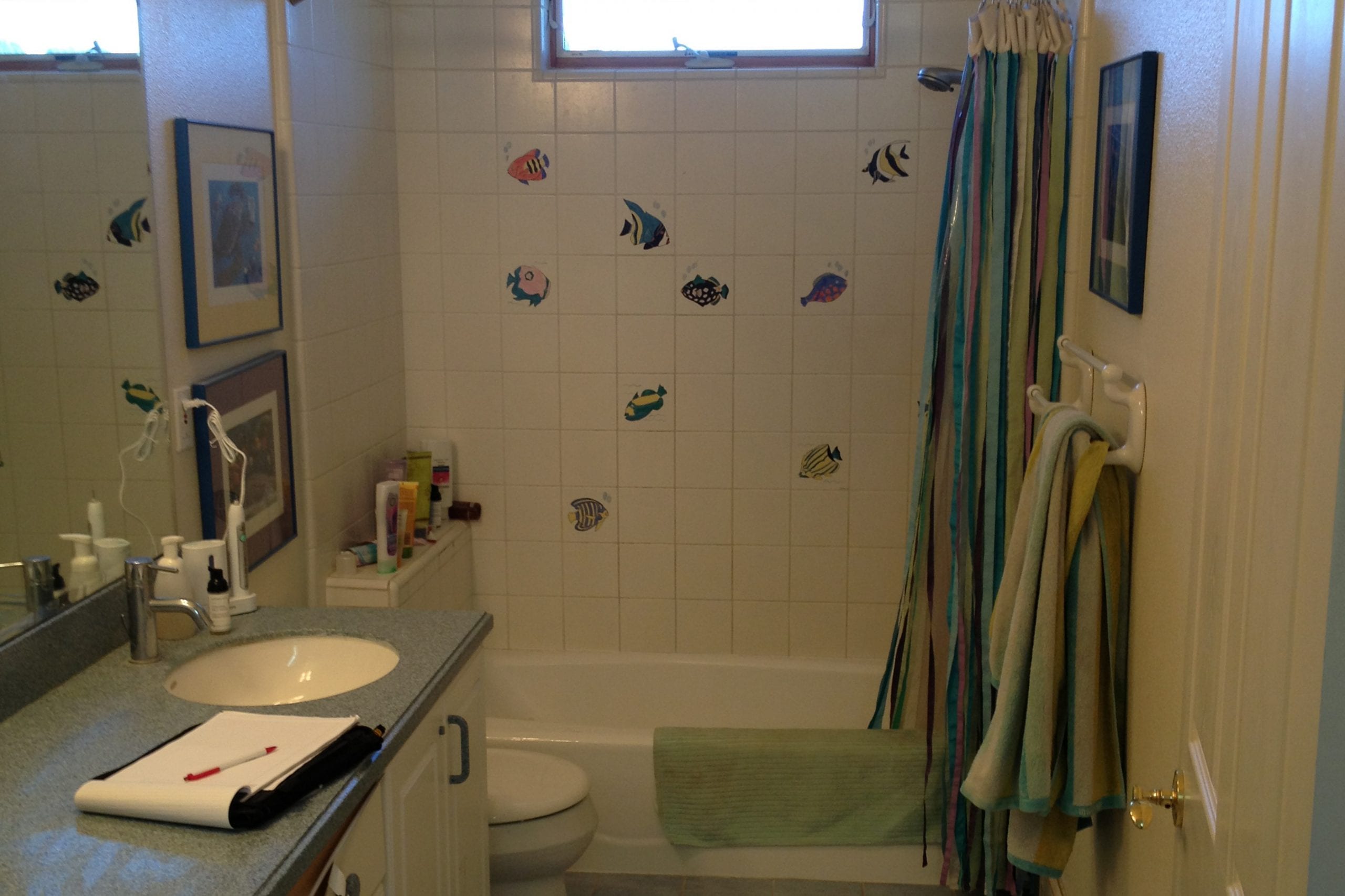 Bathroom with dim lighting, white tile, and fish stickers on the walls