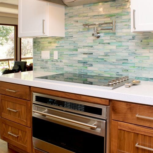 Teal tile backsplash over a white countertop and stainless steel oven