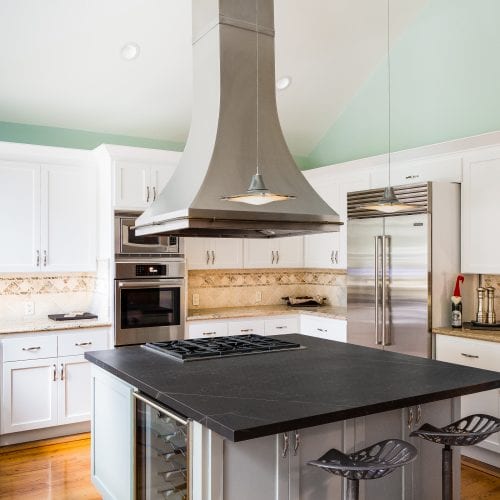 Curved metal exhaust hood over island with black granite countertop