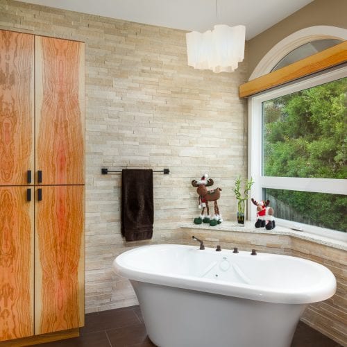 Stand alone ceramic tub next to wooden cabinets