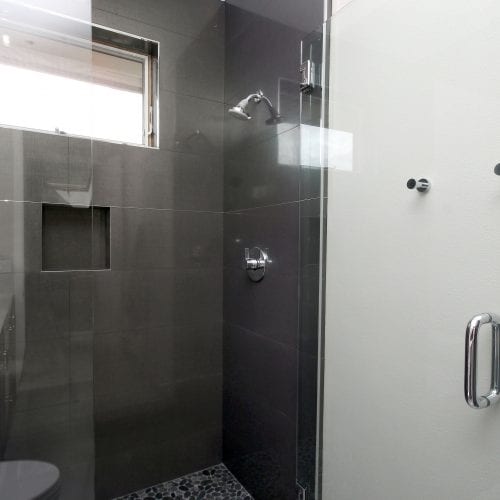 Walk-in shower featuring a swinging glass door and black tile