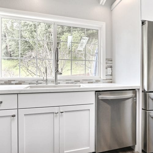 Metal finished dishwasher next to white wood cabinets