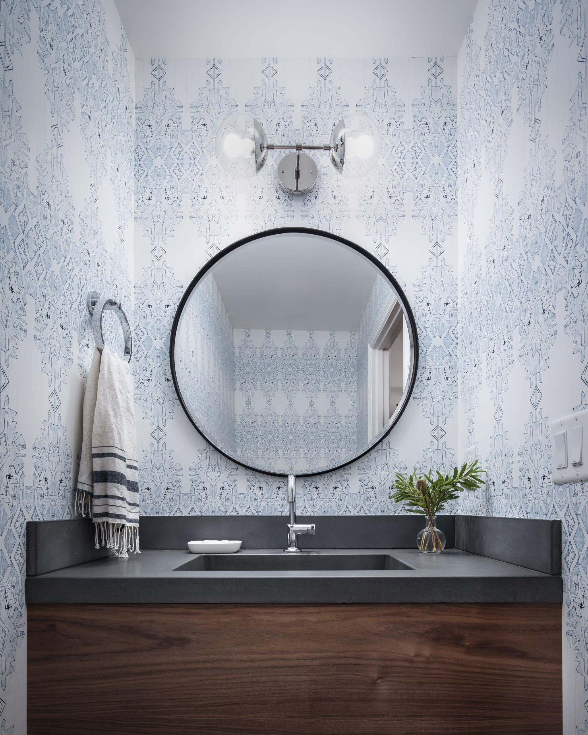 Bathroom with black circular mirror and blue and white wallpaper