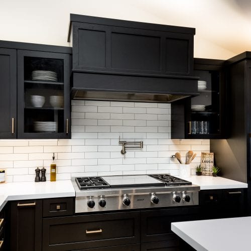 Stainless steel stove top surrounded by black finished cabinets and white tiling