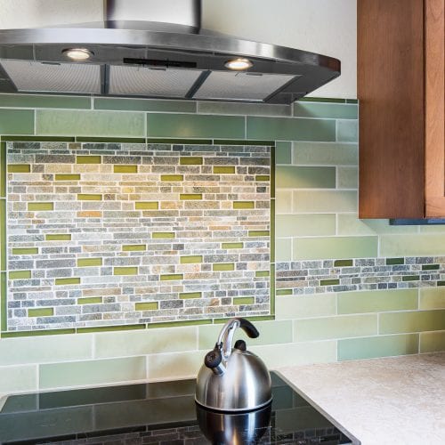 Silver teapot on electric stove in front of kitchen backsplash