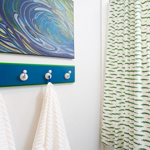 Green and white shower curtain next to blue wood towel rack