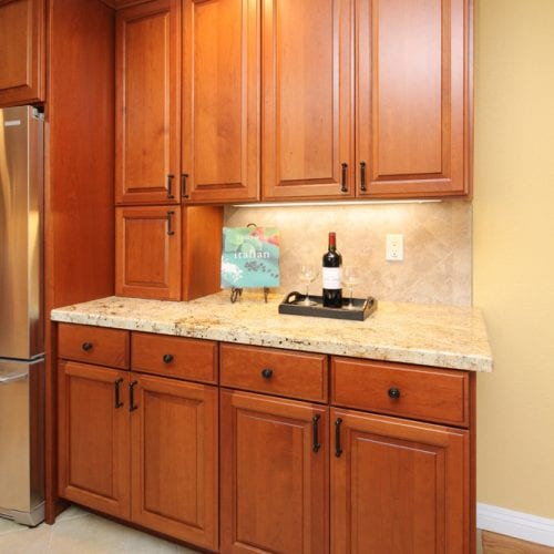 Wooden kitchen cabinets and mini-bar table next to a stainless steel fridge