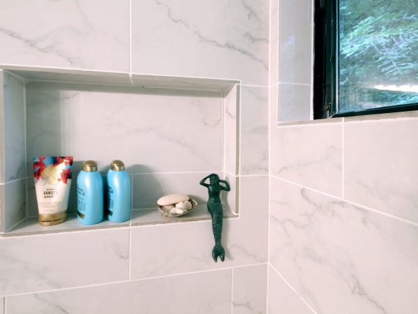 White tile shower shelf holding a mermaid and other products