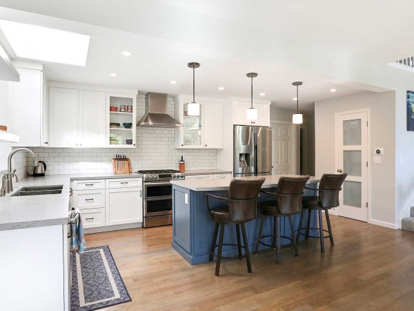 Simple kitchen with white finished cabinets, a blue island and barstools