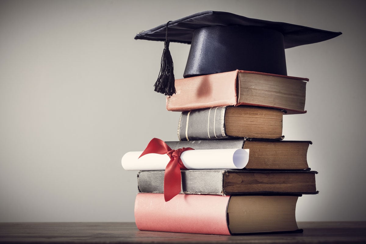 Stack of textbooks with graduation cap on top