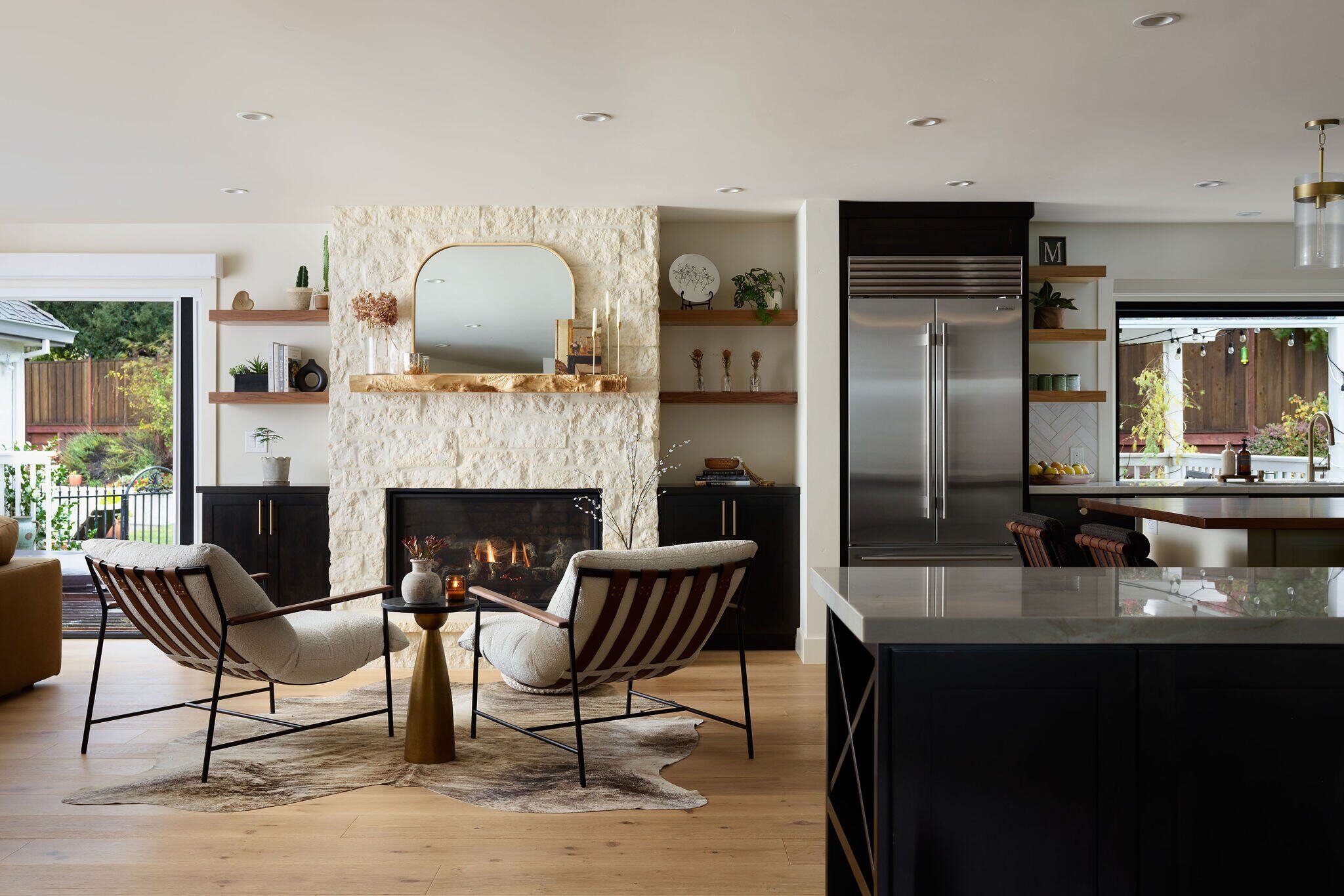 Beautiful sitting area around a white brick fireplace next to a luxury remodeled kitchen with black wood counters and stainless steel appliances