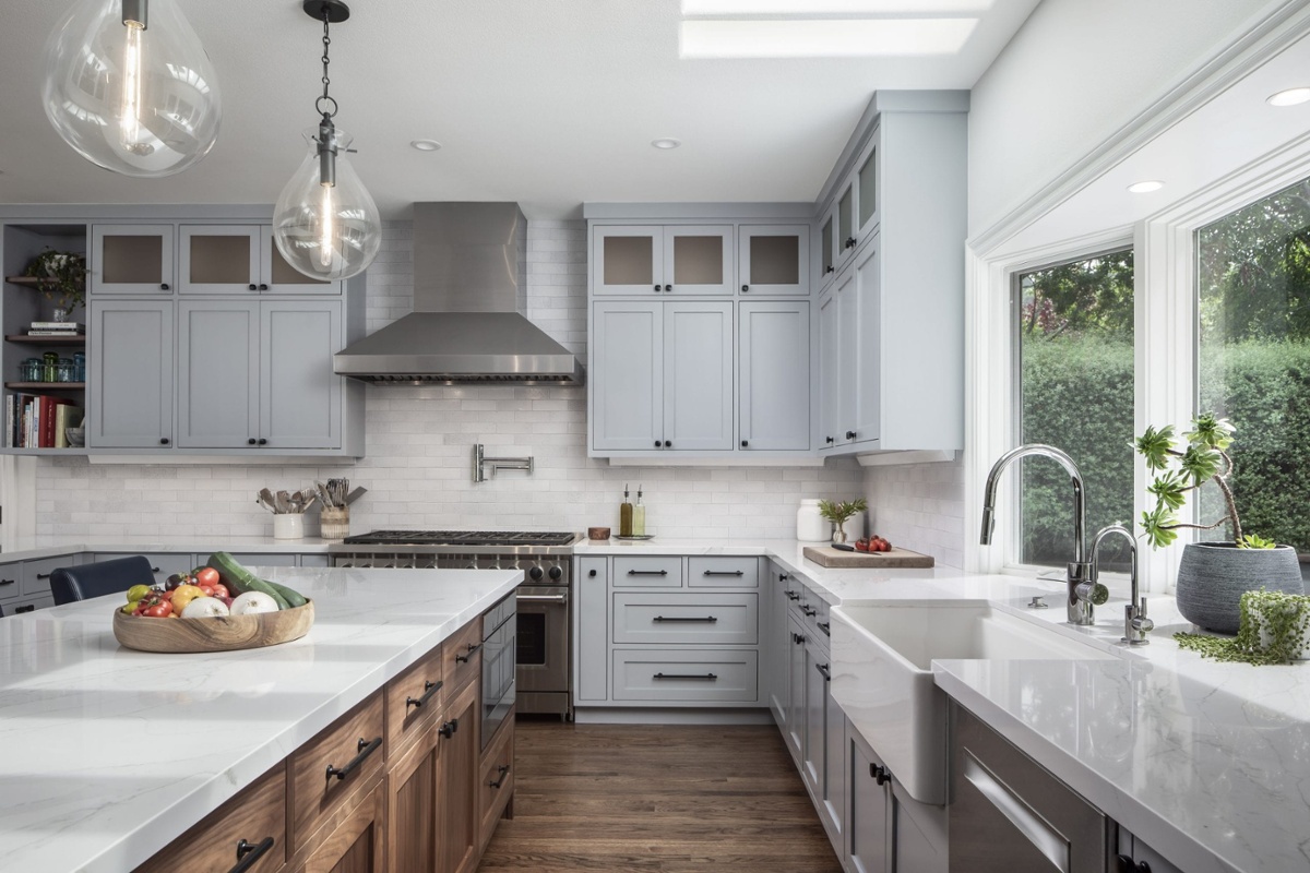 A contemporary and elegant kitchen with white countertops, white cabinetry, stainless steel appliances, and a mixture of metals for the finishes